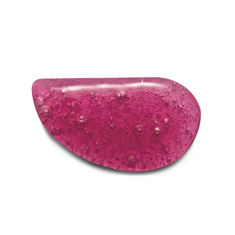 Textura do sabonete vegetal em formato oval irregular, com uma cor rosa vibrante e brilhante. A superfície apresenta pequenas bolhas e gotas de água, dando um aspecto molhado e texturizado. Não há rótulos ou texto visível.