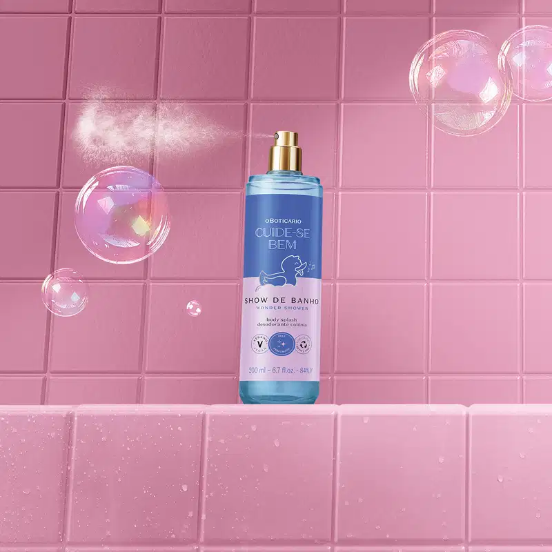 Frasco com líquido azul, pulverizador prateado, tampa transparente e rótulo azul e lilás com patinho de banho ilustrado  de body splash da marca  Cuide-se Bem Show de Banho. em ambiente rosa com bolhas de sabão flutuando ao redor.