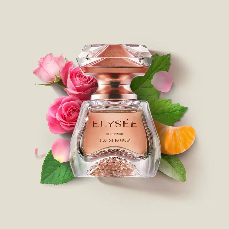 Frasco de Eau de Parfum Elysée sobre superfície clara, rodeado por rosas cor de rosa, folhas verdes e uma fatia de laranja, em cenário minimalista e claro.