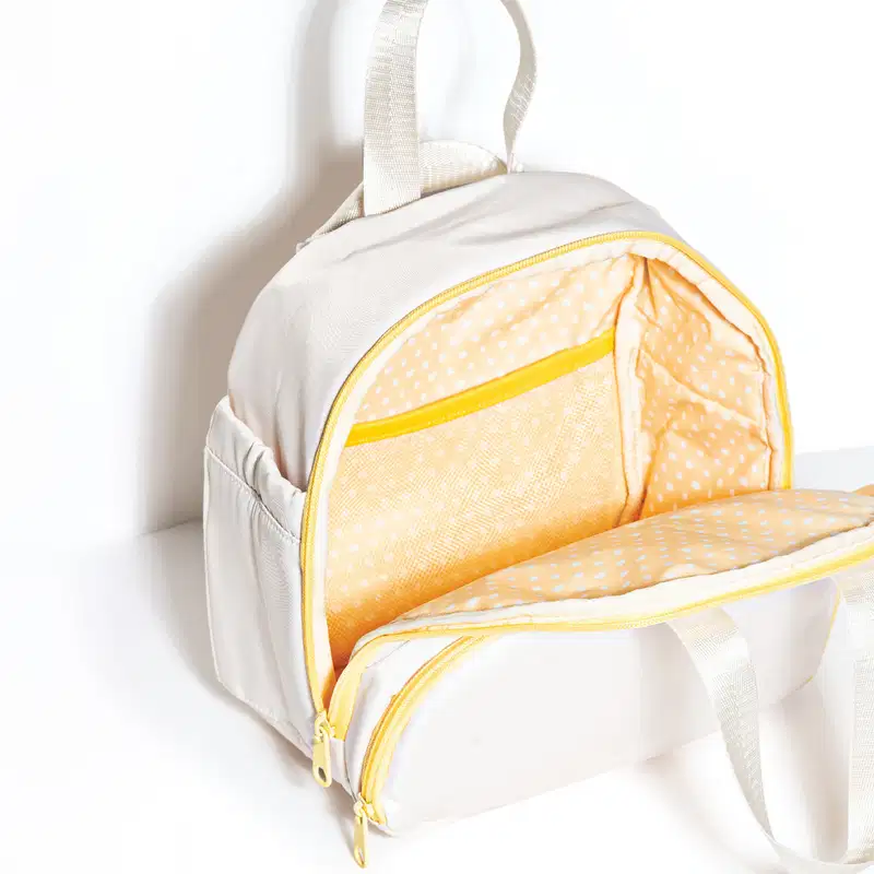 Frasqueira branca com detalhe e zíperes amarelos. Na imagem, o produto está aberto, mostrando o interior em tecido amarelo com bolinhas brancas e divisórias internas.