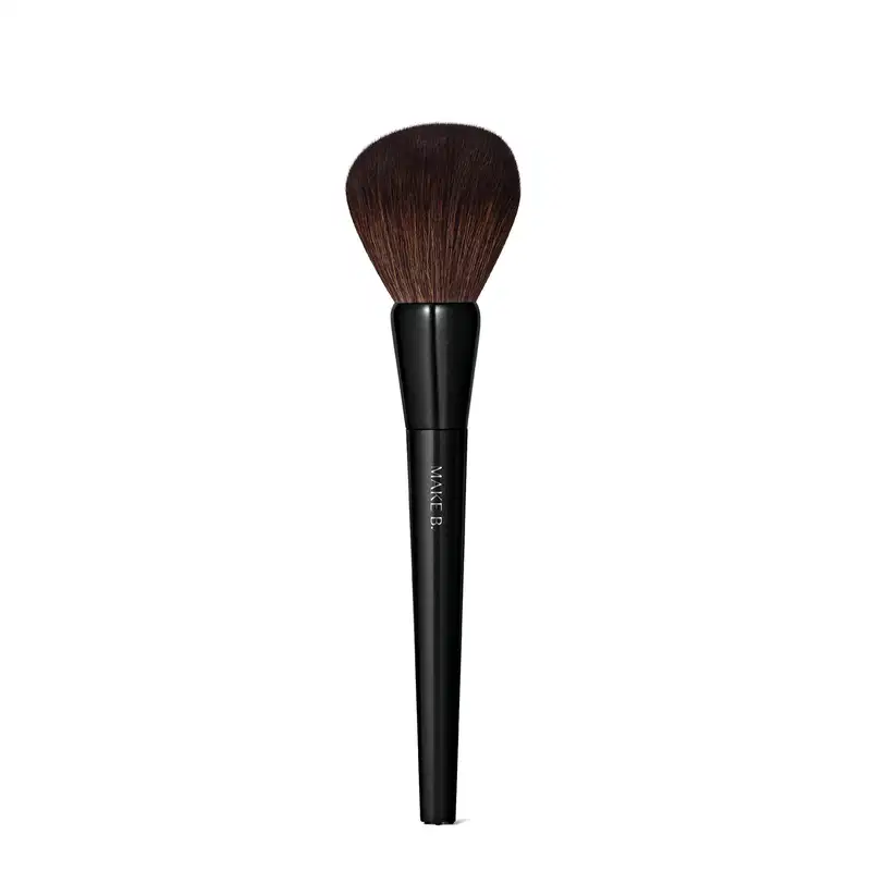 É um pincel de maquiagem de formato cilíndrico e alongado. O cabo é preto e possui o texto "MAKE B." impresso. As cerdas são macias e de cor castanha escura.  O design é simples e minimalista, com o foco no desempenho e funcionalidade do produto.