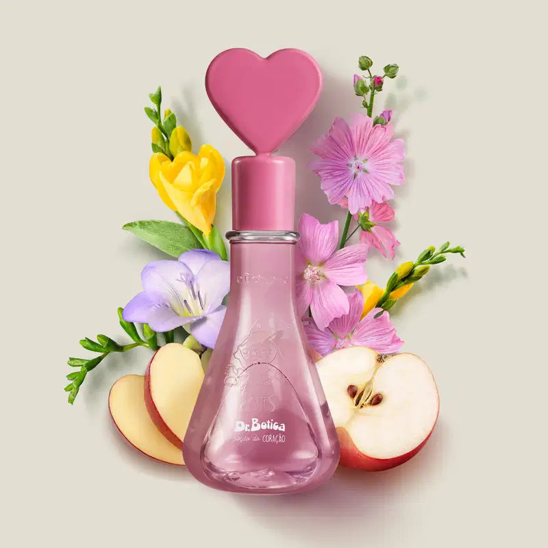 Frasco transparente com líquido rosa, tampa também rosa com coração na ponta e letras brancas no rótulo contendo colônia infantil Dr. Botica Poção do Coração rodeado por flores coloridas, frutas e folhagens em cenário claro e minimalista.