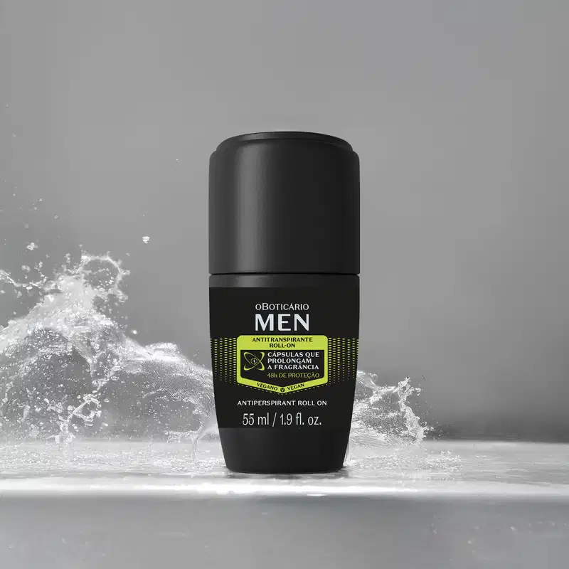 Embalagem preta com detalhes amarelos de desodorante roll-on da marca Men em primeiro plano, com respingos de água ao fundo em cenário monocromático.