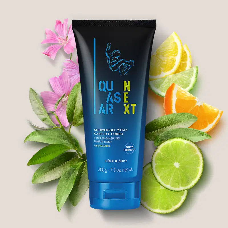 Frasco degradê de azul com preto de gel de banho para corpo e cabelo 2 em 1 da marca Quasar Next, com ilustração de skatista azul rodeado por ingredientes como rodelas de limão, fatias meia-lua de laranja, folhas verdes e flores rosas sobre fundo claro.