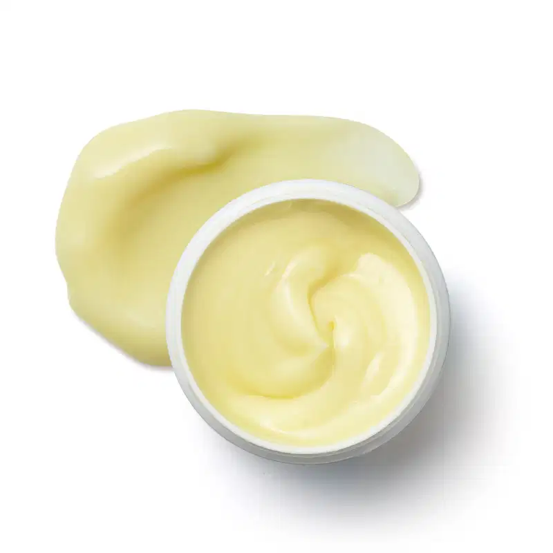 Pote branco aberto com creme amarelo dentro dele e porção de creme espalhado na superfície branca.
