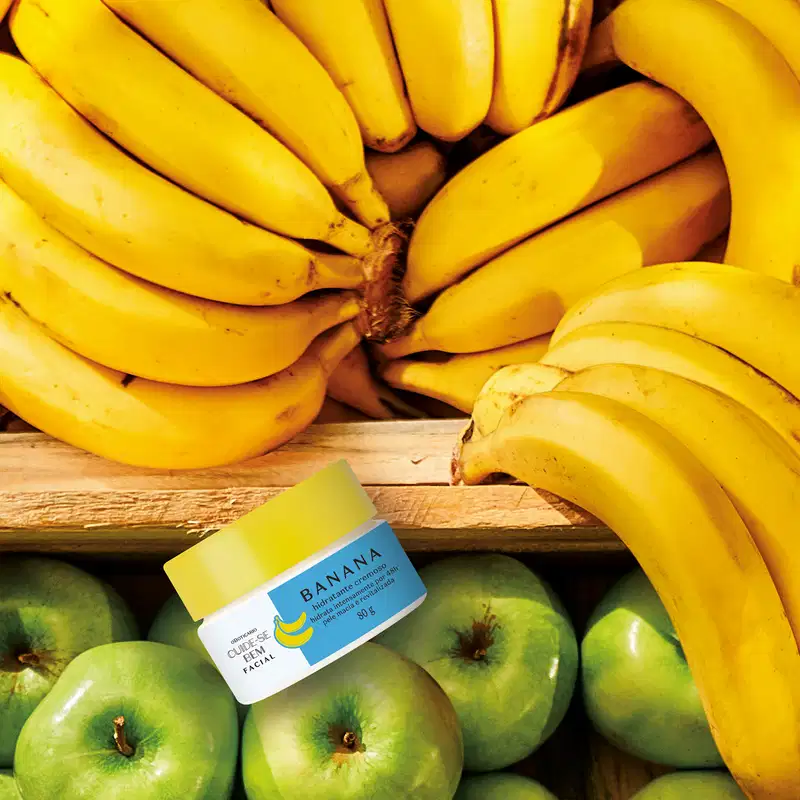 Pote branco com tampa amarela e rótulo azul com bananas amarelas ilustradas contendo creme hidratante facial Cuide-se Bem Feira Banana. em meio a bananas amarelas e maçãs verdes.