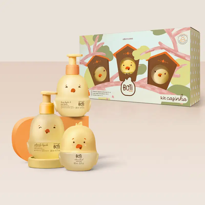 Três frascos em forma de pintinhos amarelos com detalhes laranja, sendo um de colônia do sol e outros dois com tampa dosadora laranja: um de loção banho e pós banho e o outro de sabonete líquido de glicerina. Ao lado, a caixa com ilustração de casinhas.