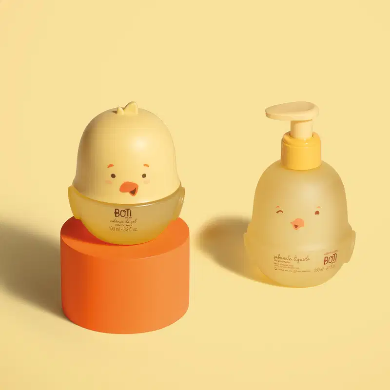 Dois frascos em forma de pintinhos amarelos com detalhes em laranja, sendo um de colônia do sol e outro, com bomba dosadora laranja, de sabonete líquido de glicerina. Os produtos estão em fundo laranja.