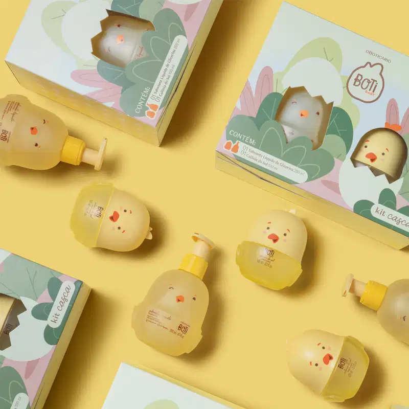 Vários frascos em forma de pintinhos de diversos itens da marca Boti Baby em meio a caixas dos produtos em fundo laranja.