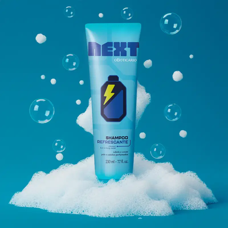 Imagem do tubo azul de shampoo Next em meio a espuma e bolhas em fundo azul. A embalagem traz imagem de bateria elétrica, indicando produto refrescante para cabelos e corpo.