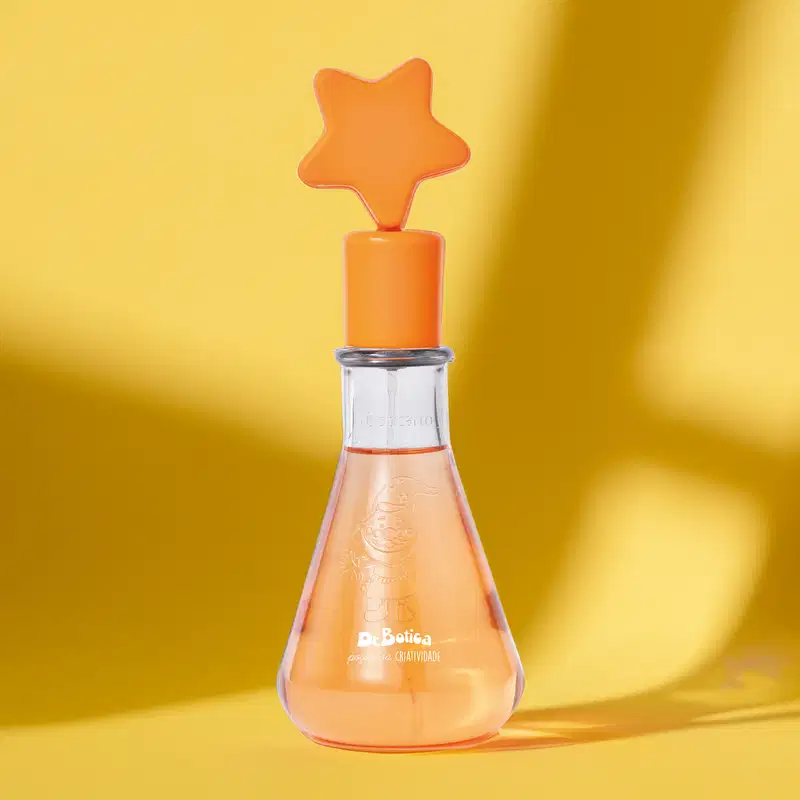 Frasco simulando um vidro laboratorial com líquido laranja e tampa com estrela na ponta também laranja contendo 120ml de colônia infantil Poção da Criatividade Dr. Botica sobre fundo amarelo brilhante, criando um ambiente vibrante e alegre.