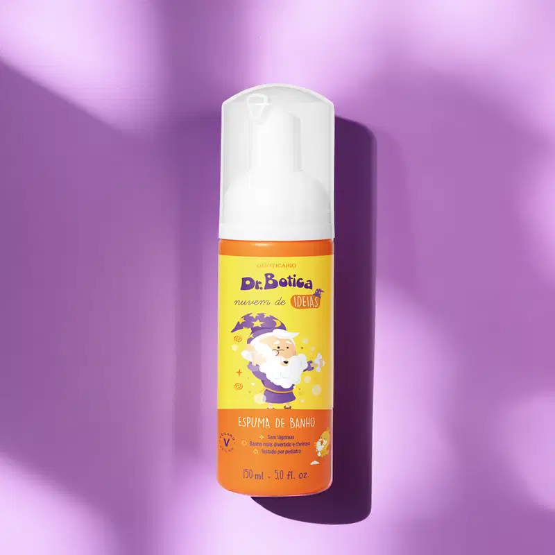 Espuma de banho corporal Nuvem de Ideias Dr. Botica em frasco com tampa branca e rótulo amarelo e laranja com ilustração do personagem da marca sobre fundo roxo com alguma iluminação natural sobre o produto.