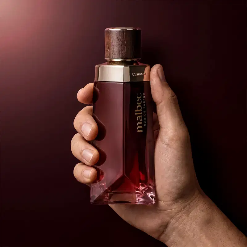 Ambiente escuro e elegante, com uma garrafa de perfume Malbec em destaque, sugerindo um contexto de luxo e sofisticação. A cor predominante é o vermelho escuro, criando uma atmosfera sensual e misteriosa.