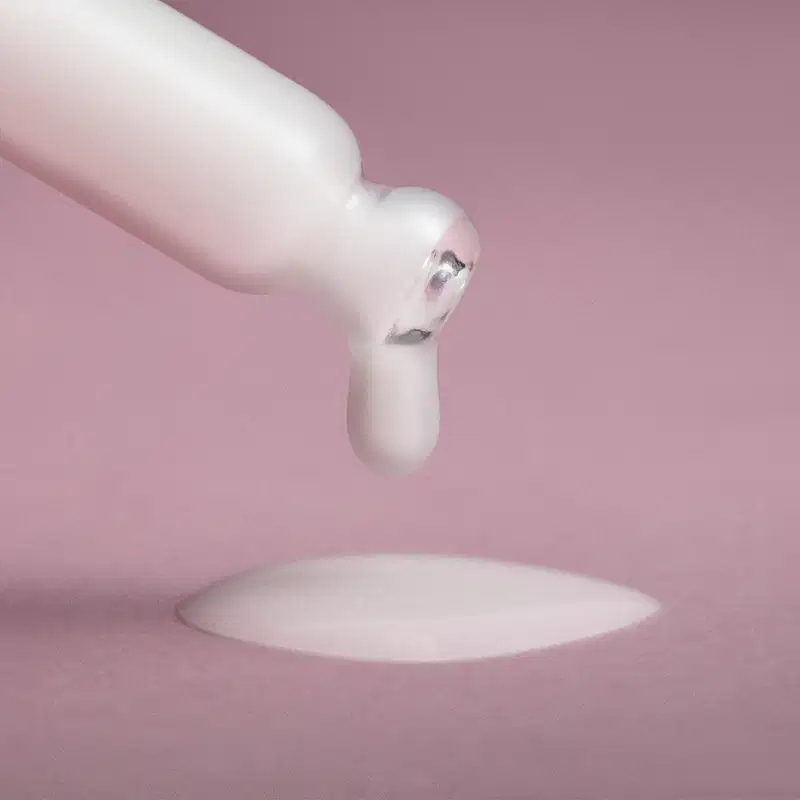 Ponta de um conta-gotas branco pingando um líquido branco não muito aquoso sobre uma superfície em tom de roxo.