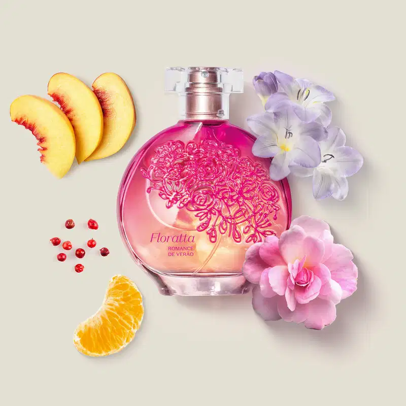Vidro redondo com líquido rosa, floral em relevo rosa escuro, pulverizador prateado e tampa transparente contendo desodorante colônia Floratta Romance de Verão com flores e fatias de frutas cítricas em superfície clara.