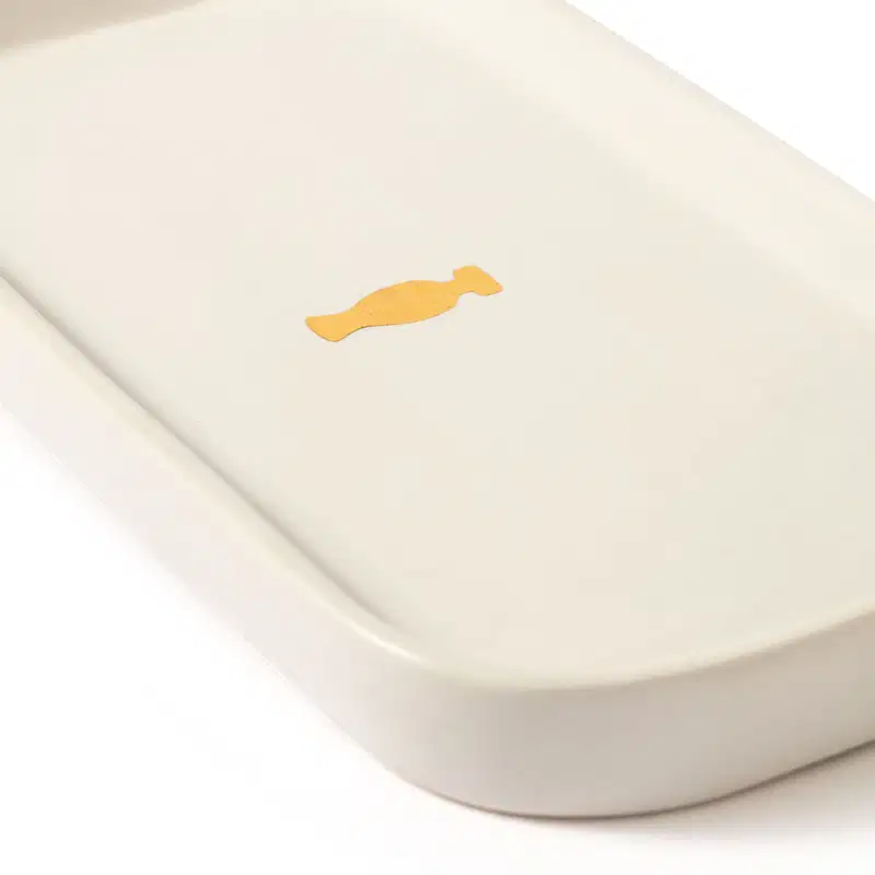 Bandeja para lavabo branca da marca Casa 214 no formato retangular com cantos arredondados e com logo do Boticário em dourado no centro.