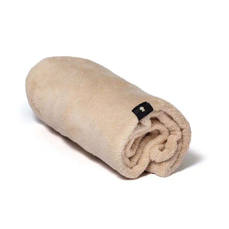 Toalha de cabelo em microfibra da marca O Boticário na cor bege e etiqueta preta com o logo da marca.