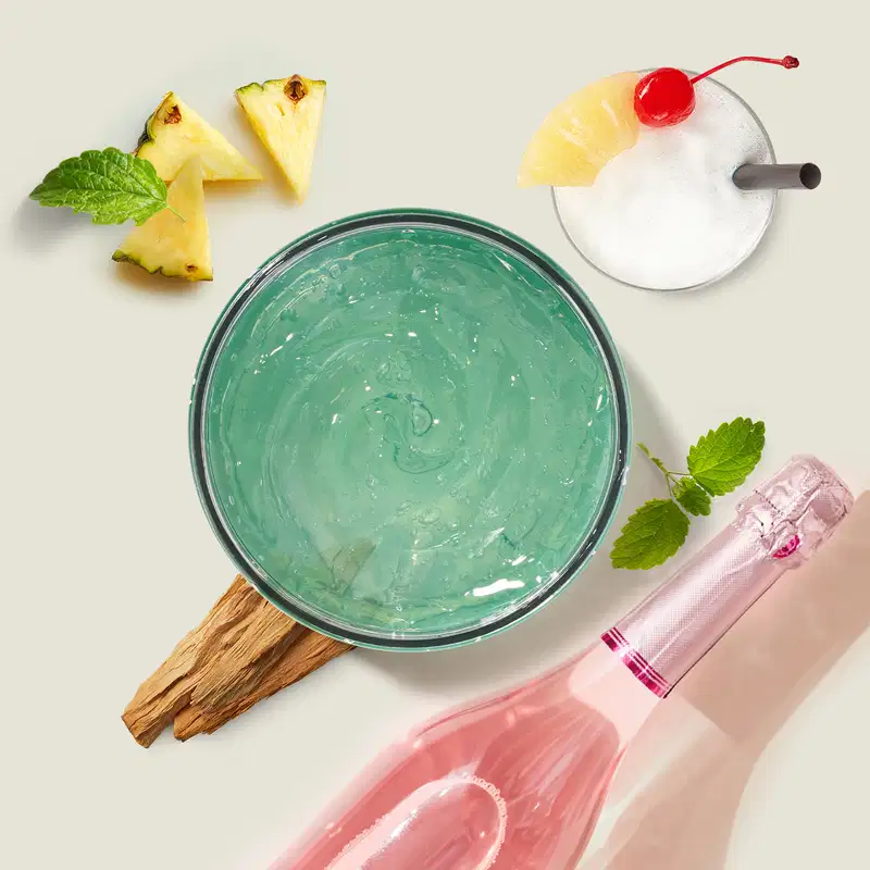 Pote de geleia desodorante refrescante corporal da marca Cuide-se Bem Bob Esponja e Amigos na cor verde, rodela de abacaxi e cereja no topo, acompanhado de pedaços de abacaxi, folhas de hortelã e uma garrafa com líquido rosa.