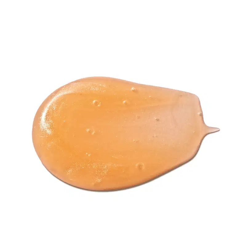 Imagem da textura gelatinosa e brilhante de tom alaranjado, com pequenas bolhas, em superfície lisa e uniforme do shampoo infantil para cabelo cachados Dr. Botica.