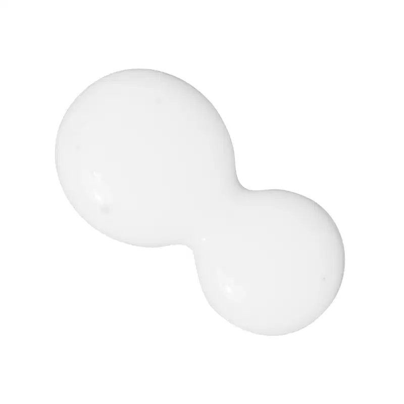 A imagem mostra algumas gotas do produto derramadas sobre uma superfície. É possível ver uma textura cremosa na cor branca, com pequenas bolhas de ar.