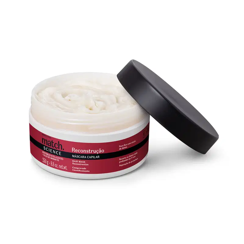 Pote branco aberto com creme branco dentro dele e tampa preta apoiada na embalagem. O produto possui rótulo na cor vermelha metalizada, preto e branco.