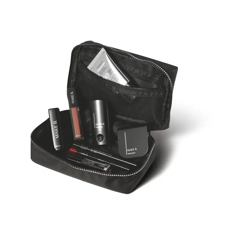 Nécessaire preta com zíper prateado aberto contendo vários compartimentos e diversos itens da marca Make B., como batom, primer, esmalte e outros produtos de maquiagem.
