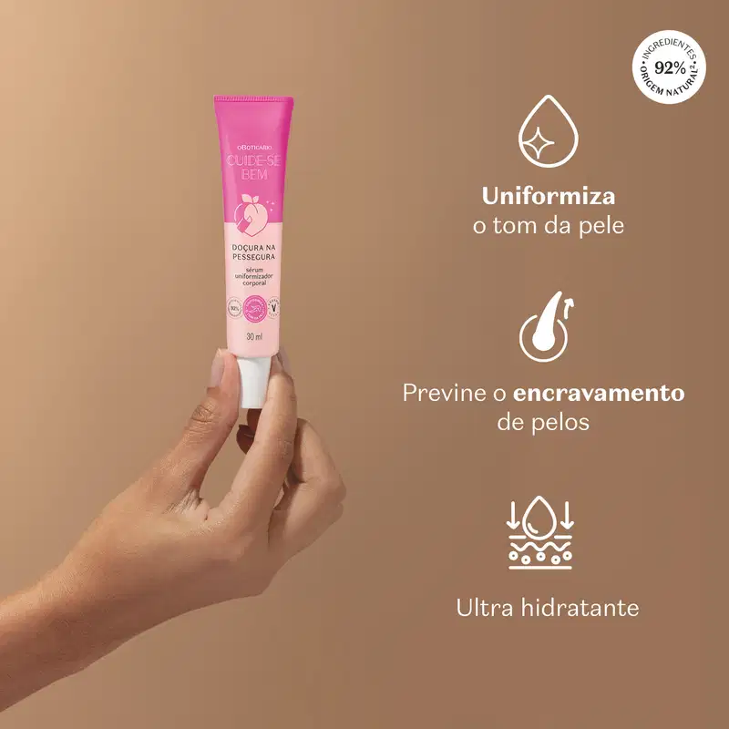 Mão feminina segurando tubo rosa de sérum uniformizador com texto branco sobre fundo bege que diz "Uniformiza o tom da pele, Premine o encravamento de pelos e Ultra hidratante".