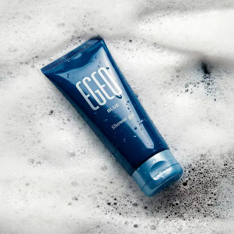 Imagem de um tubo azul marinho da marca Egeo Blue com o texto "Shower gel" sobre superfície branca com espuma.