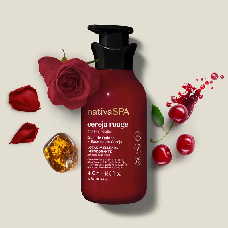 Embalagem vermelha escura de loção aveludada corporal Nativa SPA Cereja Rouge cercada por pétalas de rosa vermelha, cerejas e respingos de líquido vermelho sobre superfície clara.