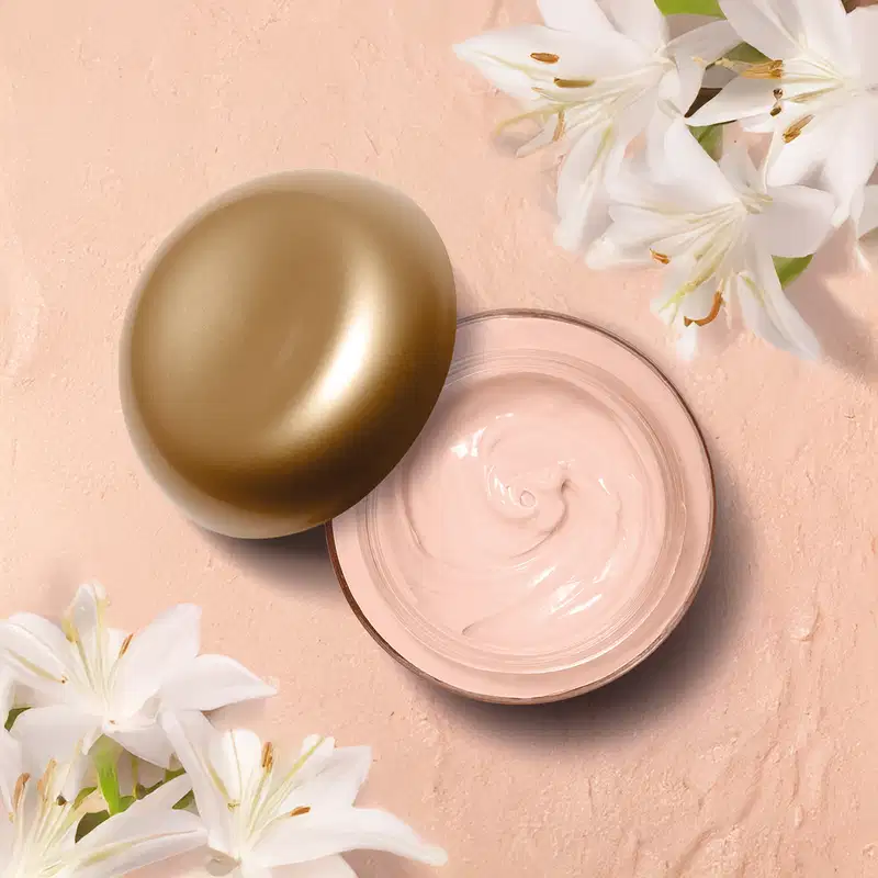 Um frasco de vidro rosa claro contendo creme acetinado corporal Lily Gardénia. Flores brancas de lírio ao redor, criando um arranjo natural e elegante.