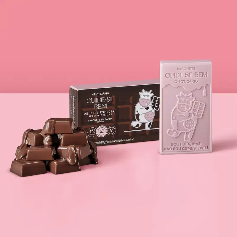 Sabonete em barra de chocolate com embalagem especial. Embalagem marrom com ilustração de uma vaca usando um avental e segurando uma barra de chocolate. Sabonete com ilustração de uma vaca e texto "Sou fofa, mas não sou comestível!".