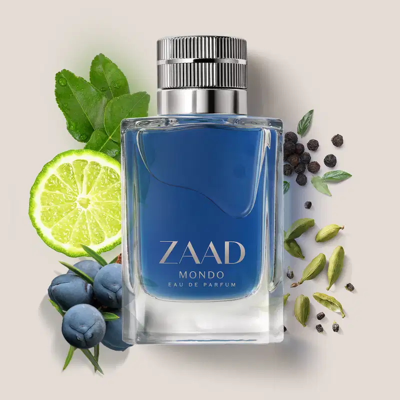 Frasco de vidro transparente de item de perfumaria da marca Zaad Mondo, contendo líquido na cor azul, tampa prateada e marca gravada no rótulo, também em prata em meio a ingredientes naturais como limão, folhas, especiarias e frutas, em superfície clara.