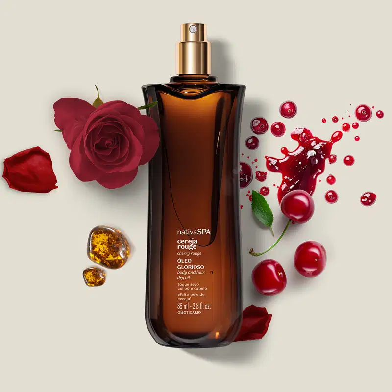Frasco de vidro vermelho com tampa dourada. Rótulo indica "nativa SPA cereja rouge óleo glorioso ". Acompanhado por rosas vermelhas, cerejas, folhas e pedras âmbar. Embalagem de 85ml. Cores predominantes são vermelho, dourado e âmbar.