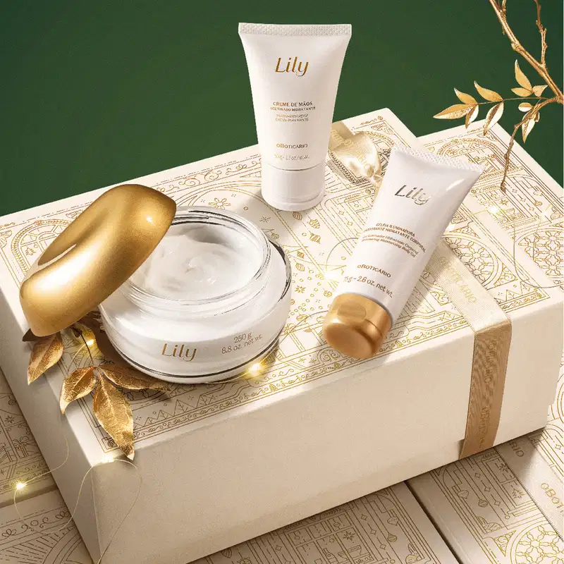 Caixa de presente bege com detalhes dourados e três itens da marca Lily em embalagens na cor branca e dourada, incluindo creme de mãos acetinado, geleia iluminadora corporal e creme acetinado corporal. em fundo verde escuro.