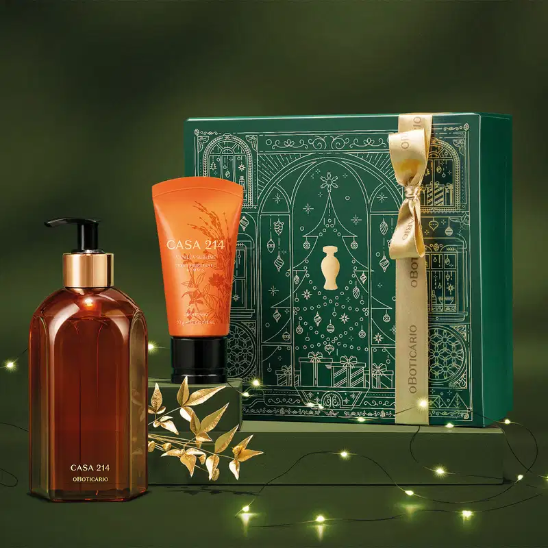 Caixa verde com detalhes dourados e dois itens Casa 214 Vanilla Sublime: bisnaga laranja com tampa preta de creme hidratante de mãos e um vidro laranja com bomba dosadora preta de sabonete líquido em fundo verde com luzes de natal e flor dourada.