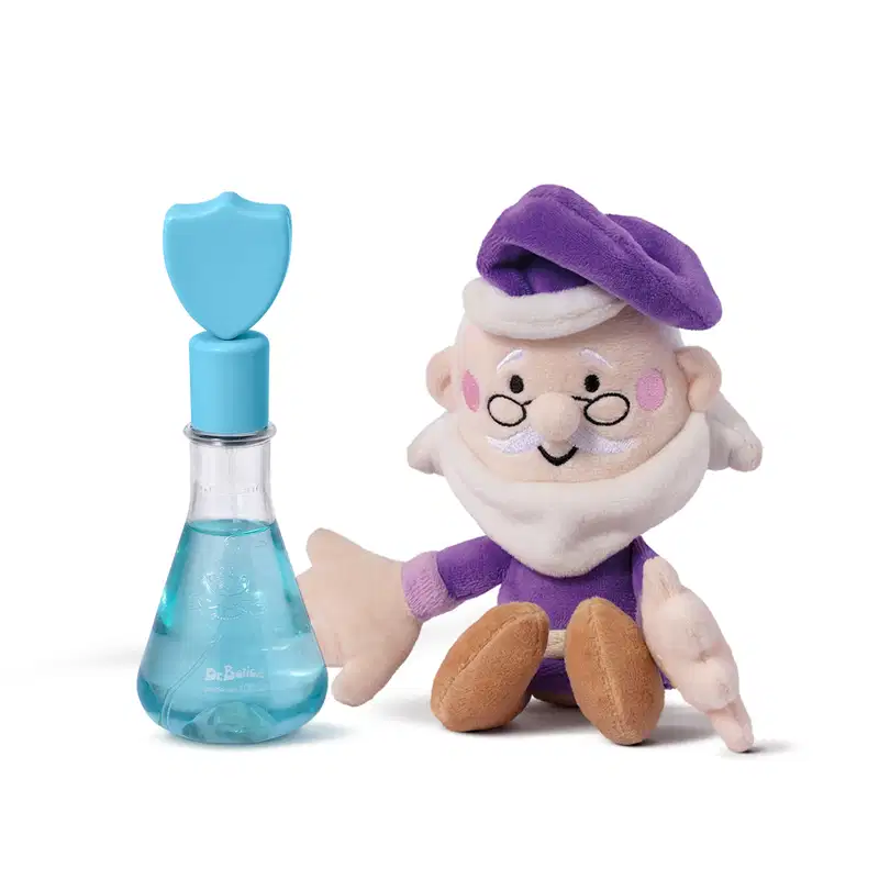 Pequeno boneco de pelúcia com roupa roxa e chapéu, ao lado de um frasco de vidro azul com tampa azul em formato de escudo de colônia infantil Poção da Coragem da marca Dr Botica.