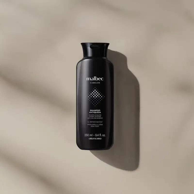 Frasco preto com letras brancas e detalhes cinza contendo 250ml de shampoo antiqueda Malbec Cabelos em fundo bege com sombras.