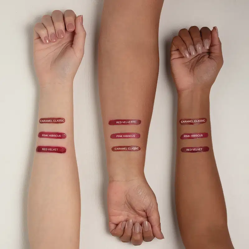 Imagem mostra três braços de cores diferentes estendidos sobre superfície branca sendo o braço mais a direita de pele negra, o do meio de pele parda e o da esquerda com pele branca, todos com diversos tons de batom aplicados sobre eles e seus códigos.