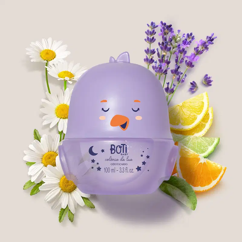 Embalagem da colônia Boti Baby Lua em formato de pintinho na cor lilás rodeada por flores de camomila, lavanda, fatias de limão e laranja em fundo claro.