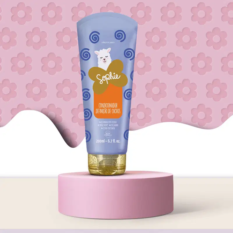 Imagem de uma embalagem azul  de condicionador para cabelos com ilustração de lhama e espirais azul escuro da linha Sophie sobre pedestal redondo rosa em fundo lilás de flores rosa, criando um ambiente minimalista e delicado.