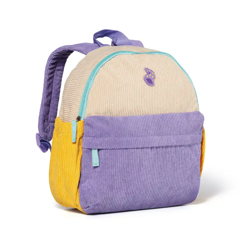 Mochila infantil de veludo canelado nas cores bege, lilás e amarelo, com zíper e aplicação de ícone em formato de touca de mago na parte frontal. Vista 45 graus.