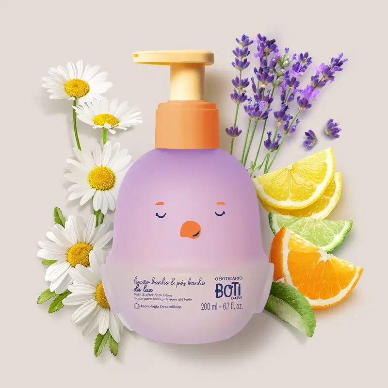 Embalagem de loção para banho e pós banho Boti Baby Lua em formato de pintinho na cor lilás e tampa dosadora laranja rodeada por flores de camomila, lavanda, fatias de limão e laranja em fundo claro.