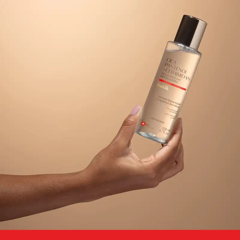 Frasco de água micelar reparadora da marca Botik Cica Pantenol e Ceramidas sendo segurado por mão feminina sobre fundo bege.