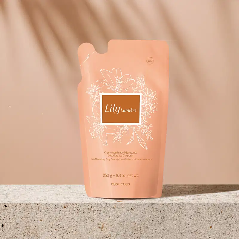 Refil de creme acetinado hidratante corporal da marca Lily Lumière em sachê de 250g na cor rosa com rótulo bege escuro, detalhes e letras douradas, posicionada sobre superfície cinza clara, com parede bege e sombras de luz natural ao fundo.