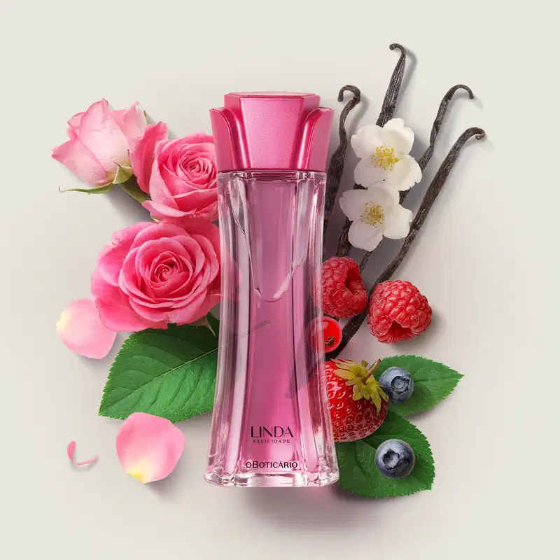 Frasco de vidro com líquido rosa e tampa rosa em formato de flor contendo desodorante colônia Linda Felicidade em meio a rosas, framboesas, baunilha e flores brancas sobre superfície clara.