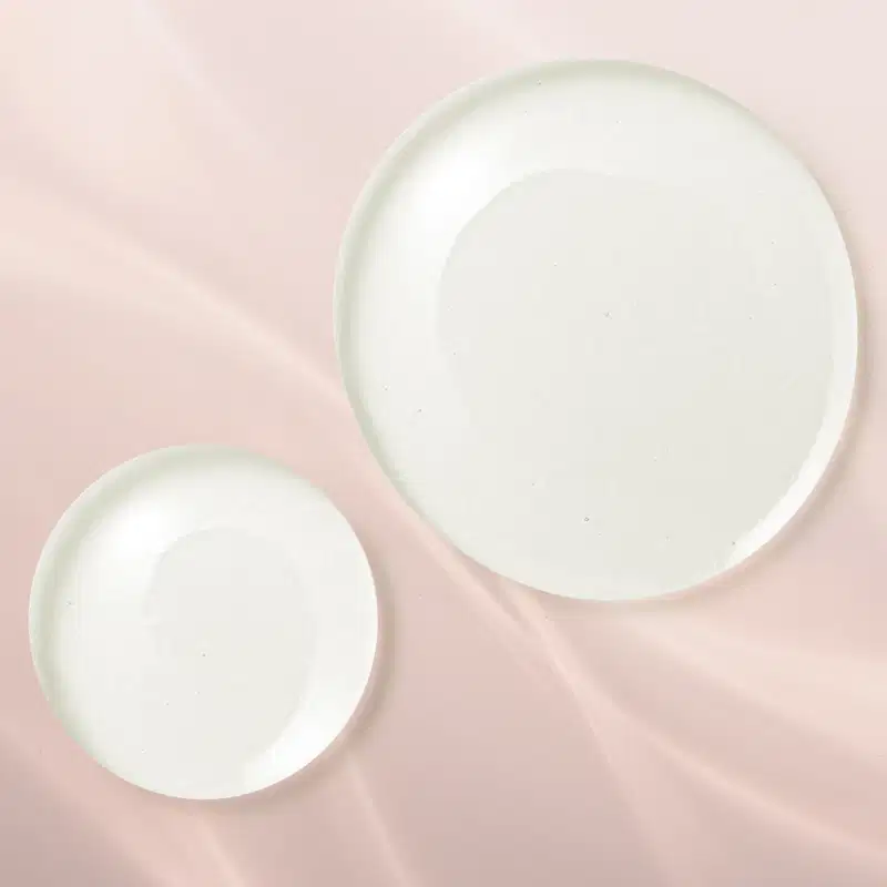 Duas gotas aquosas e transparentes mostrando a textura do elixir facial Make B. em fundo rosado.