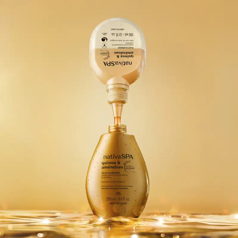 Imagem de uma embalagem refil de óleo glorioso corporal da marca Nativa SPA Quinoa e Amêndoas derramando o produto dentro de um frasco dourado de óleo corporal da mesma marca. O fundo da imagem é bege vibrante e a superfície molhada está molhada.