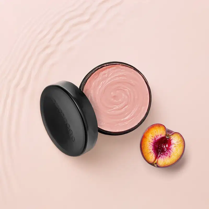 Tampa preta do óleo em creme corporal Nativa SPA Ameixa com creme rosado em recipiente aberto, acompanhado de ameixa cortada ao lado, em fundo rosa claro, sugerindo um ambiente de cuidados de beleza e bem-estar.