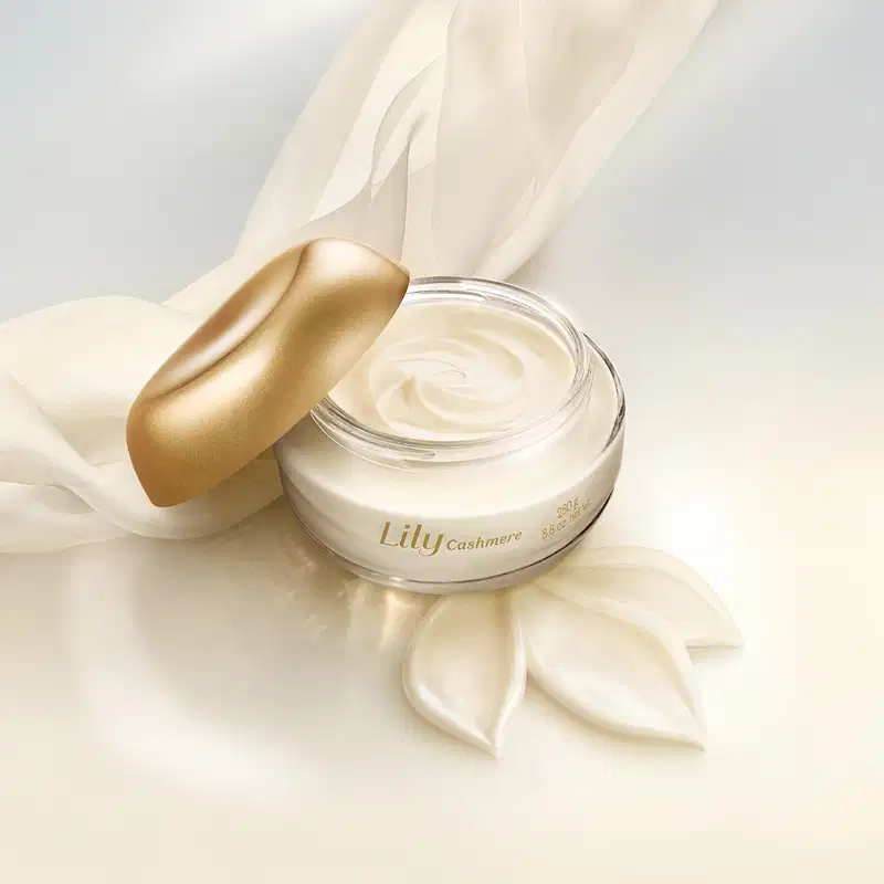 Imagem do creme acetinado corporal Lily com textura cremosa e coloração branca. Possui consistência suave e aveludada, indicando uma fórmula hidratante e nutritiva. A embalagem está aberta em um ambiente com creme espalhado por todos os lados.