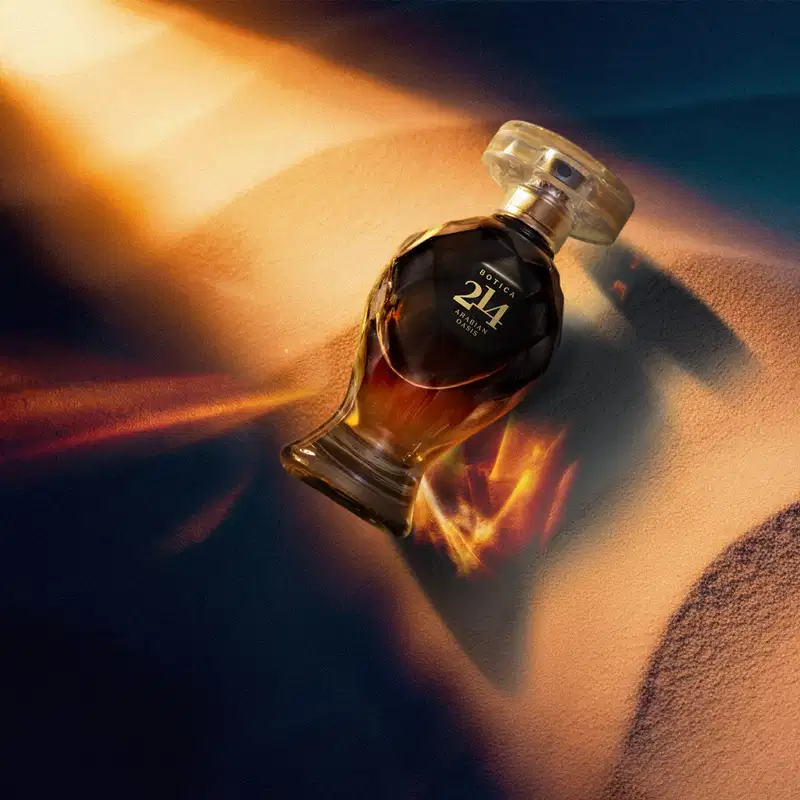 Frasco de item de perfumaria da marca Botica 214 Arabian Oasis em primeiro plano, sobre uma superfície de areia ondulada, com fundo desfocado feixes de luzes douradas que criam um ambiente misterioso e dramático.